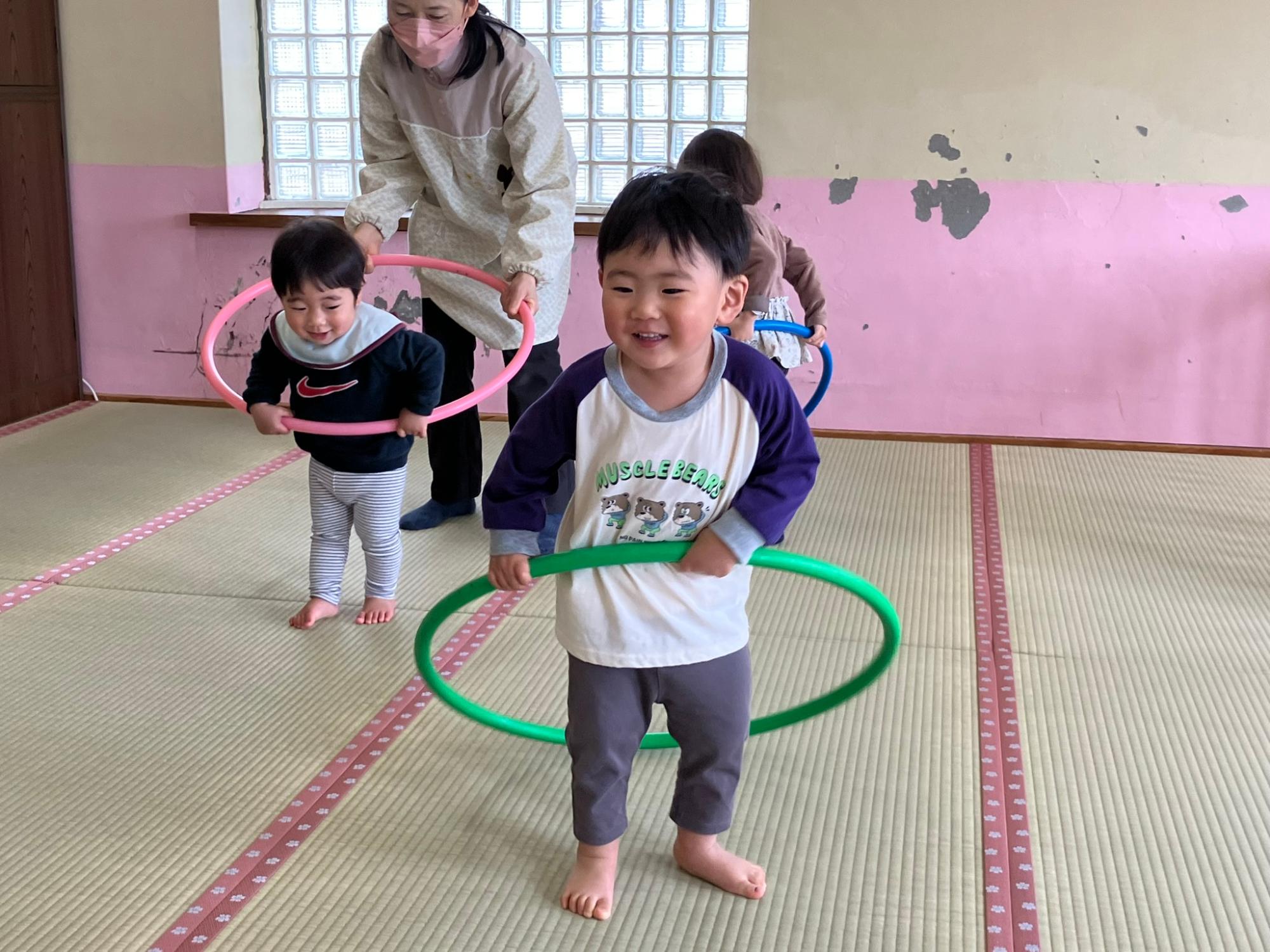 保育室でフラフープで遊ぶ2歳児と1歳児の男の子