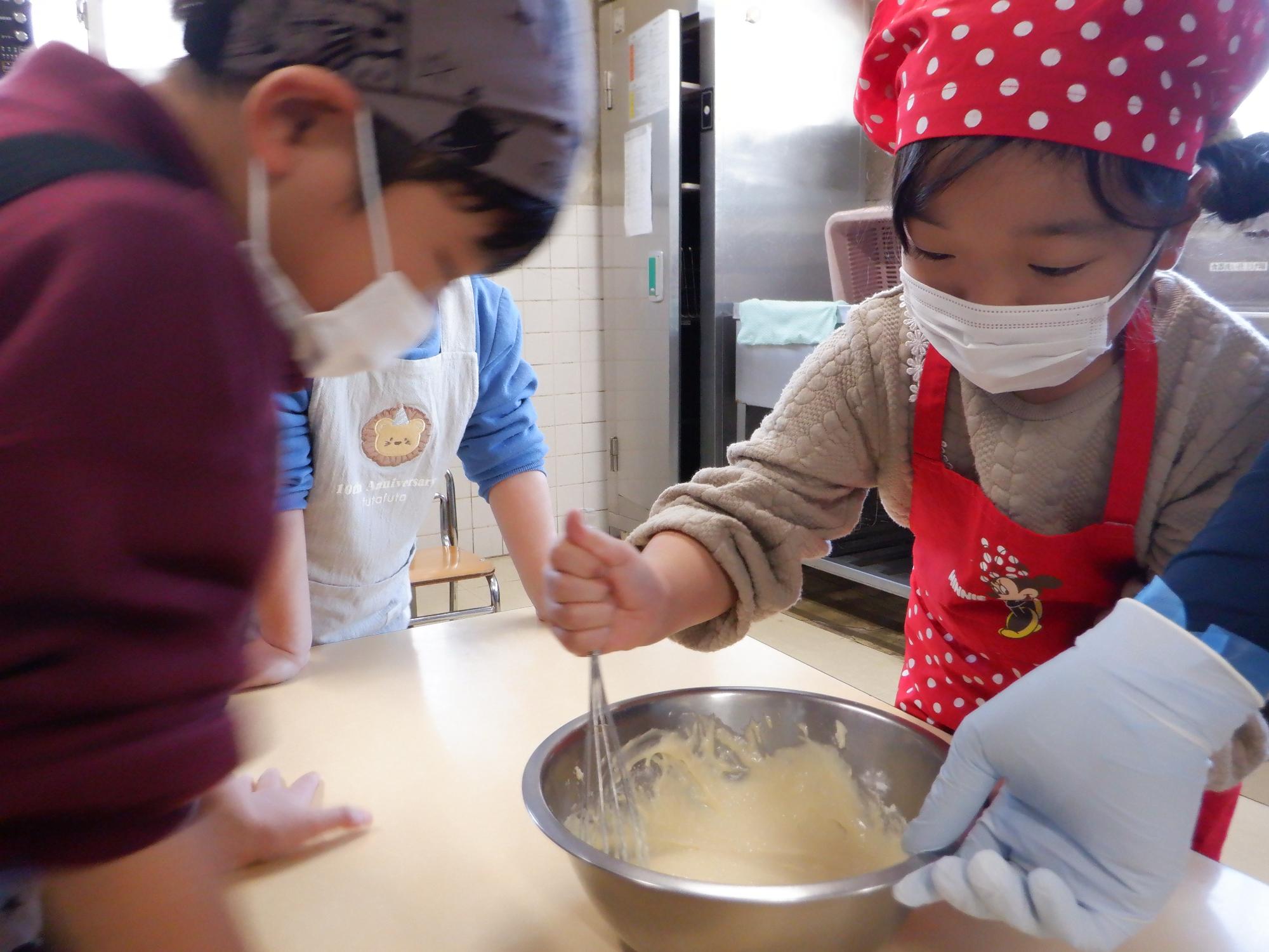ホットケーキの種作り、ボールの材料を泡だて器で混ぜる子ども
