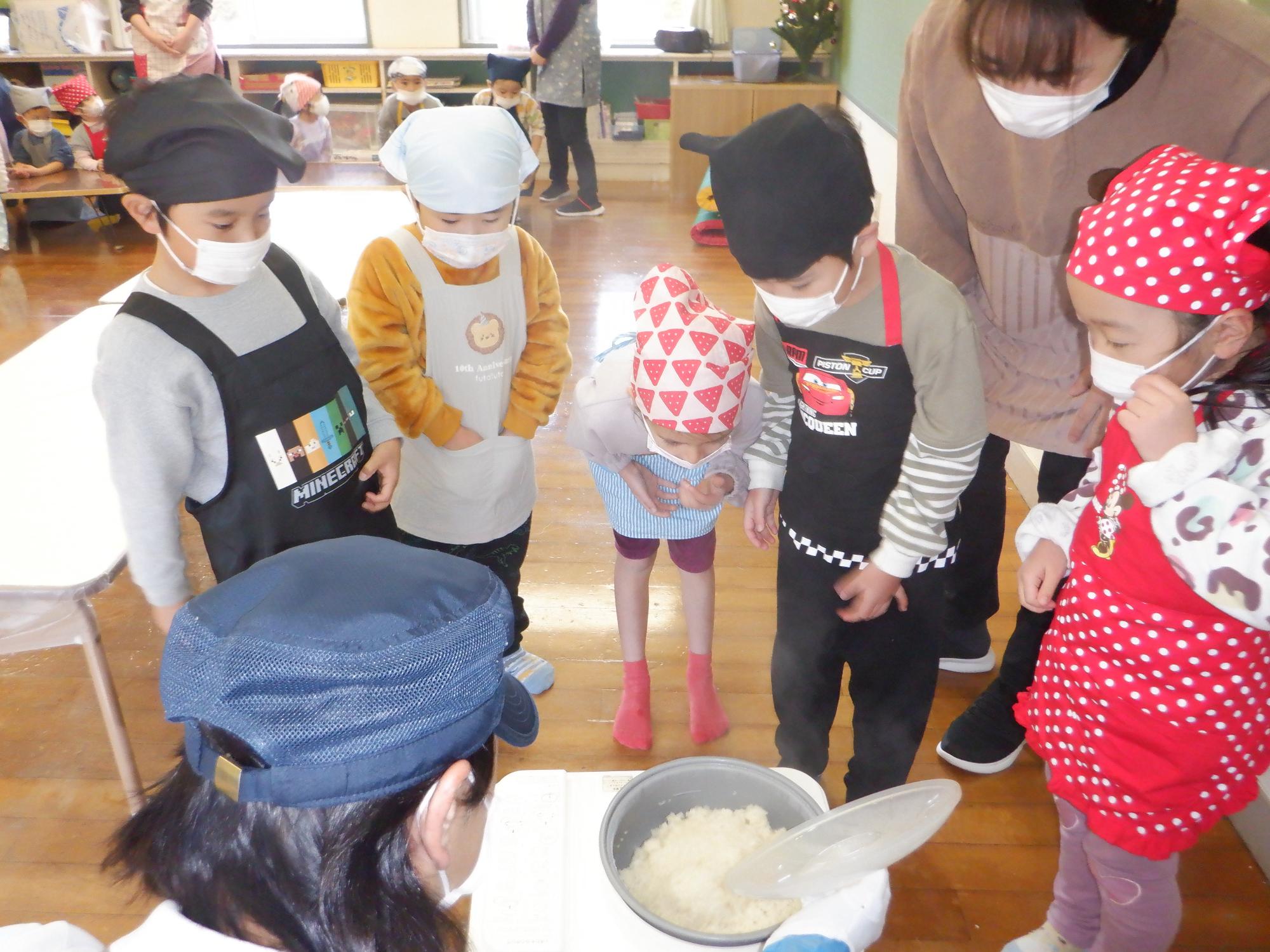餅つき機の周りに集まって、お餅になる様子を見る子ども達、まだもち米の粒がある