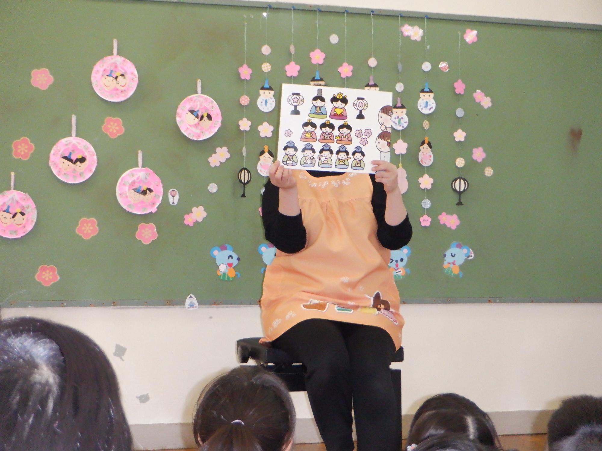 ひな祭りの由来の紙芝居です、保育者が子ども達に読み聞かせをしています
