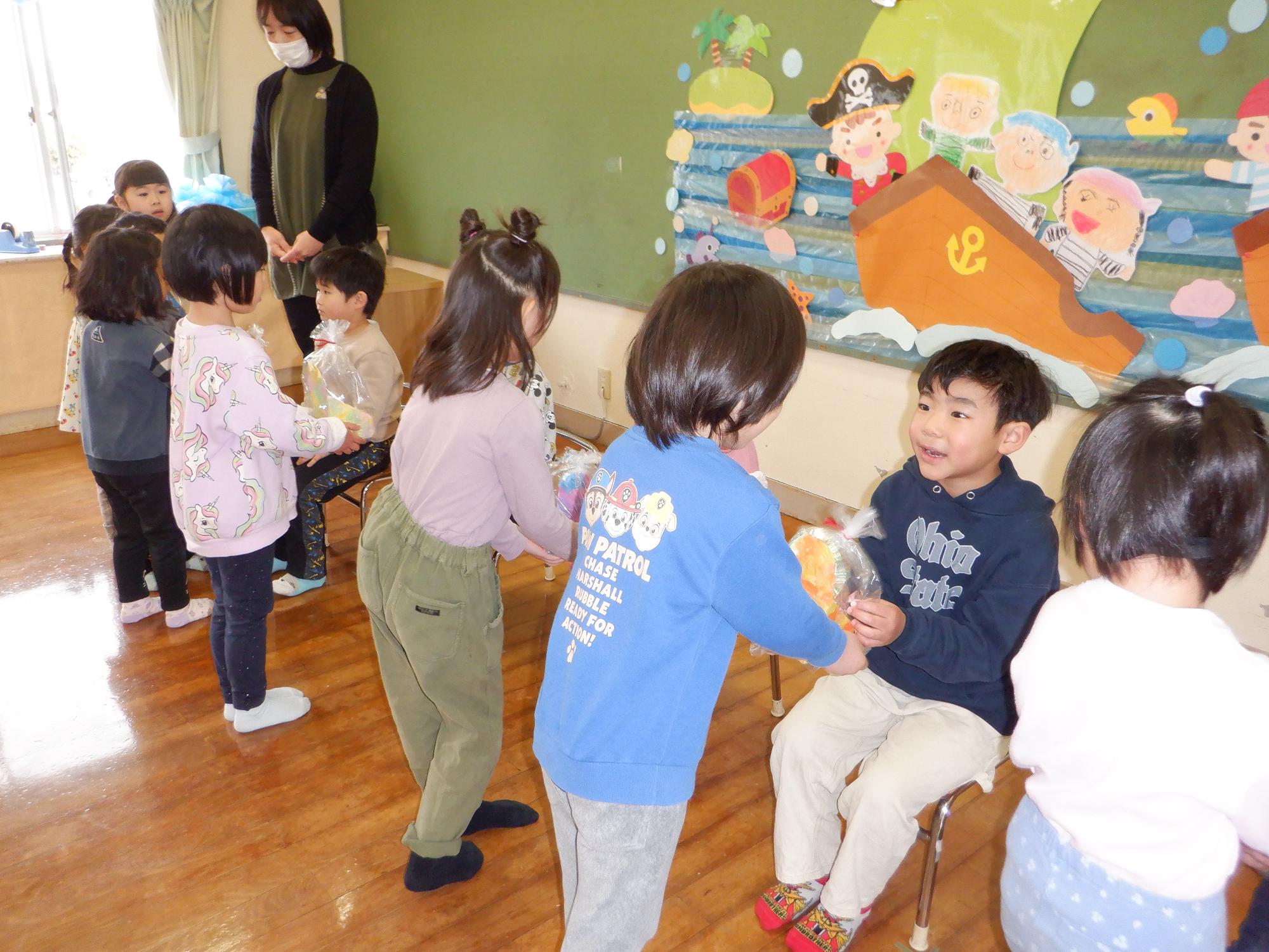 在園児の子どもから卒園児にプレゼント渡す、座っている園児に小物入れのプレゼント