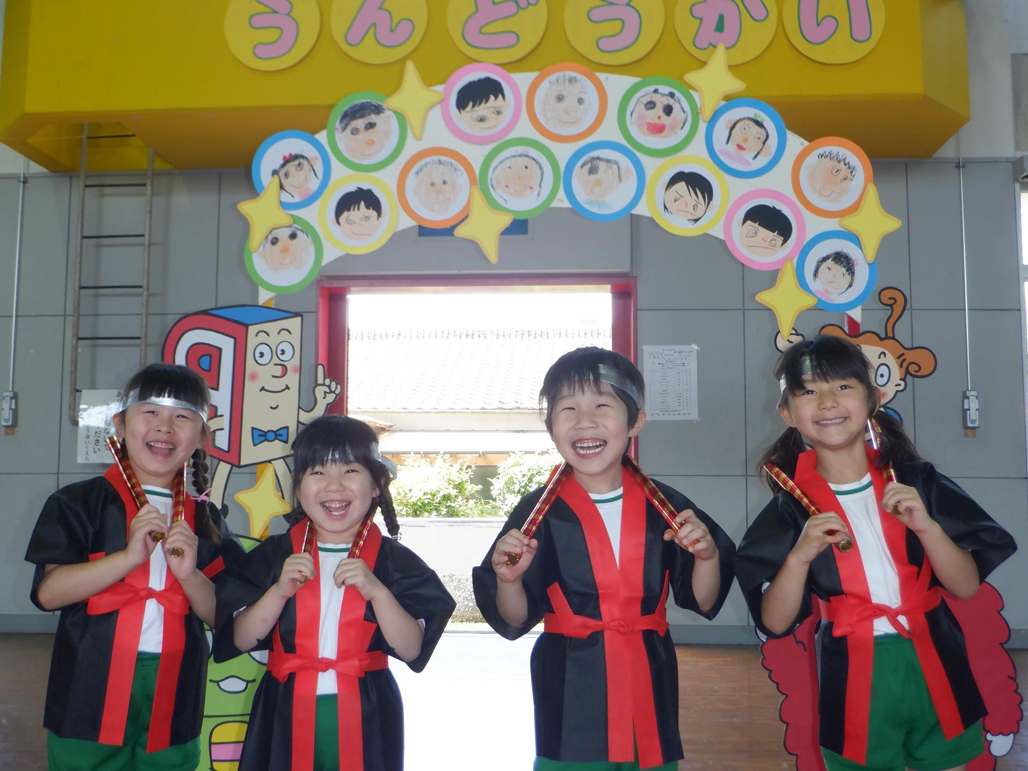法被に鉢巻を付けた子どもたち、キラキラのばちを持って肩にかけている、皆ニッコリ笑顔