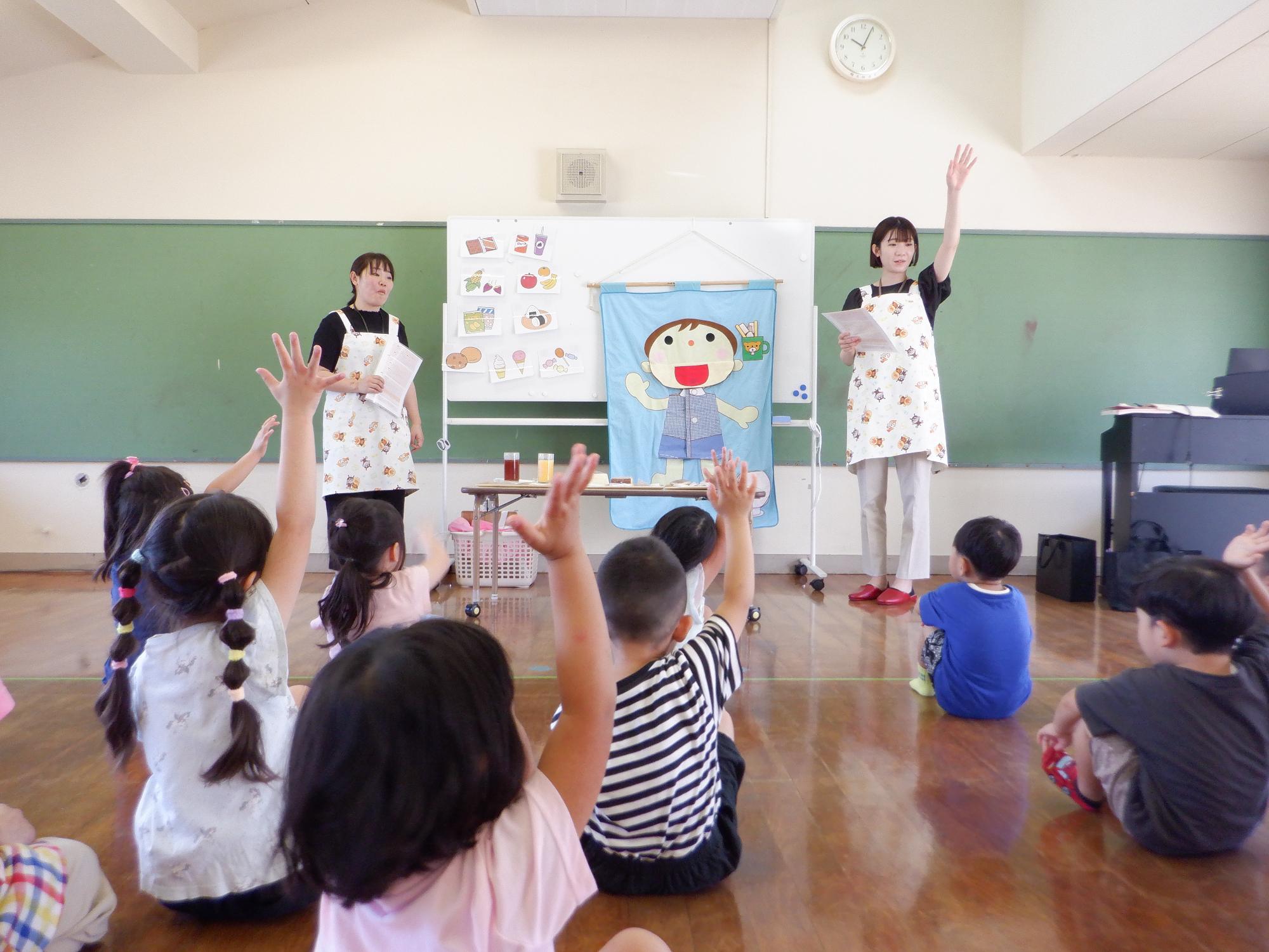 歯の健康についての質問に手を挙げて意見を言おうとしている子どもたち、前ではボードを使ってお話をする保健師さん達
