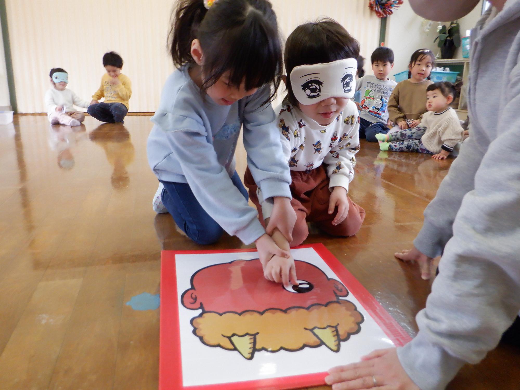 福笑い(鬼）子ども2人一組で目の位置を決めて置いている。