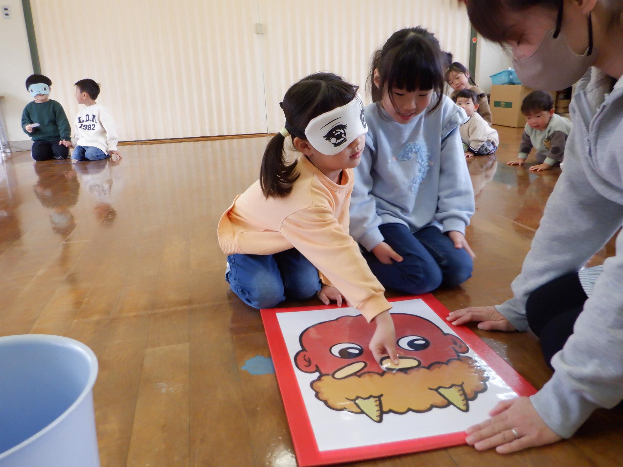 鬼の福笑いを二人の女の子がしている。眉毛を置いている。