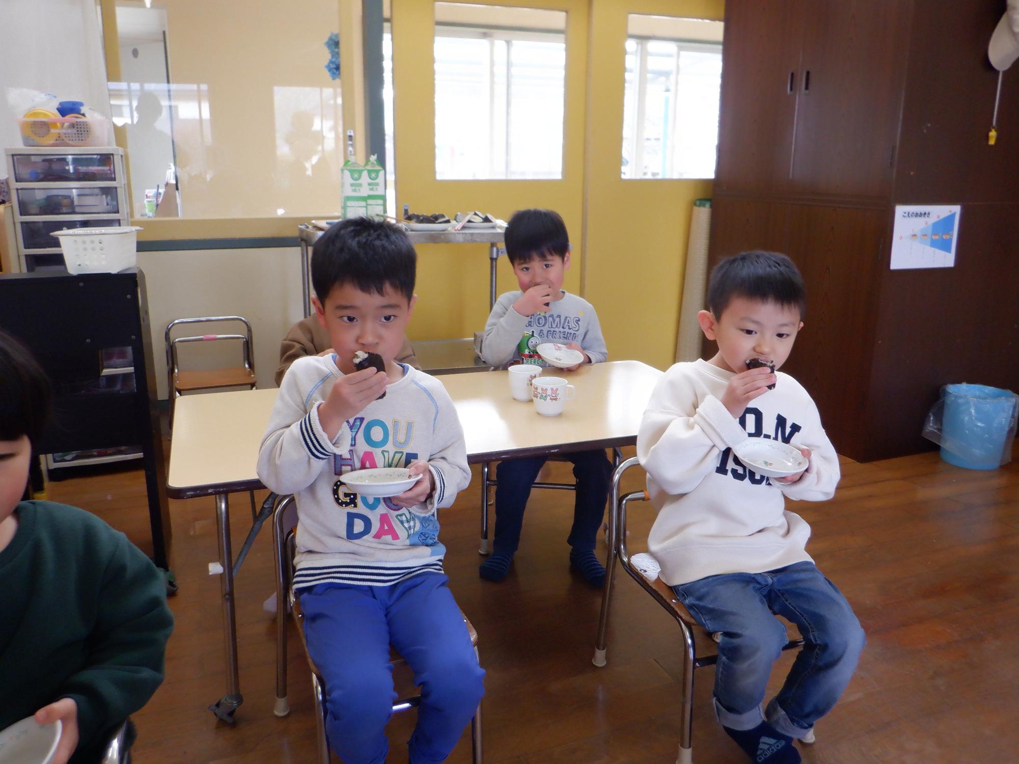 恵方巻を食べる子ども達、手に巻き寿司を持ち同じ方向を向いて食べている