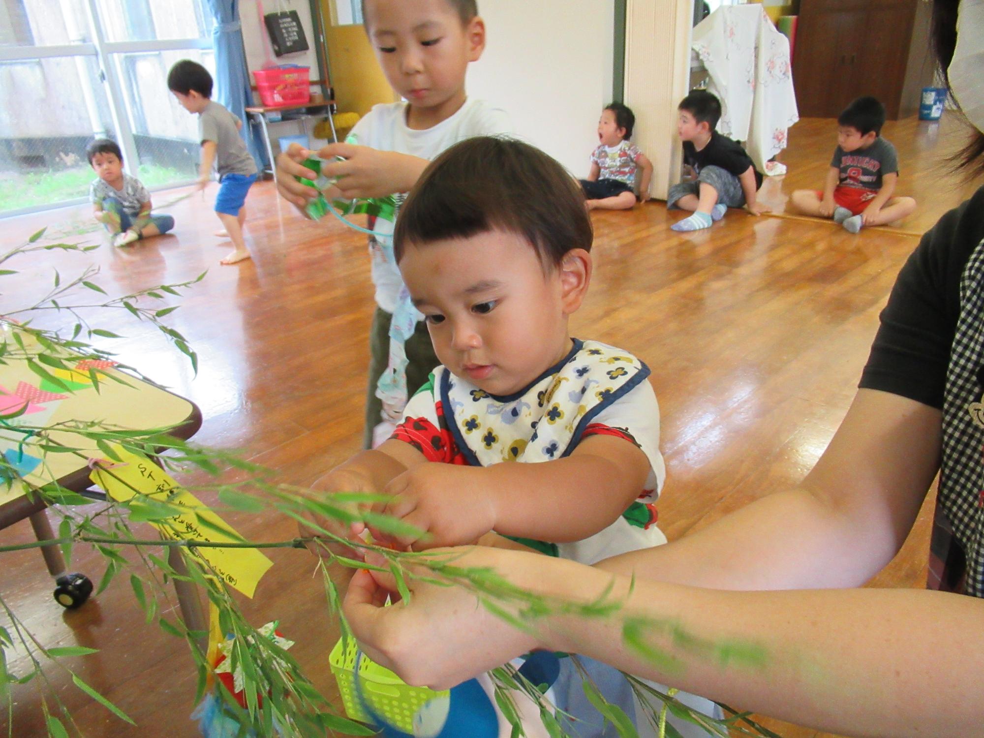 保育者に援助され真剣な表情で飾りをつけている男の子