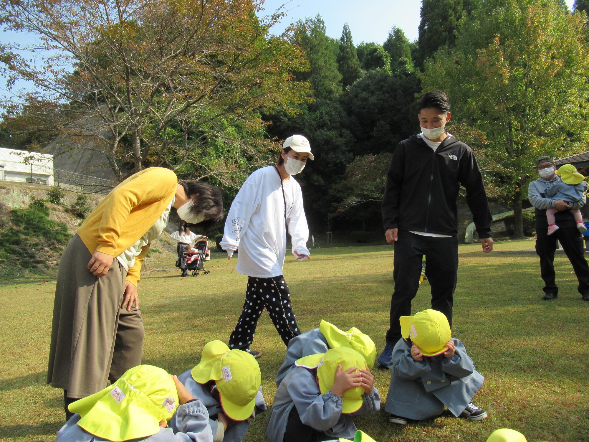 子どもたちが顔を伏せてかくれんぼ。お家の人は我が子はどこだと探してる。