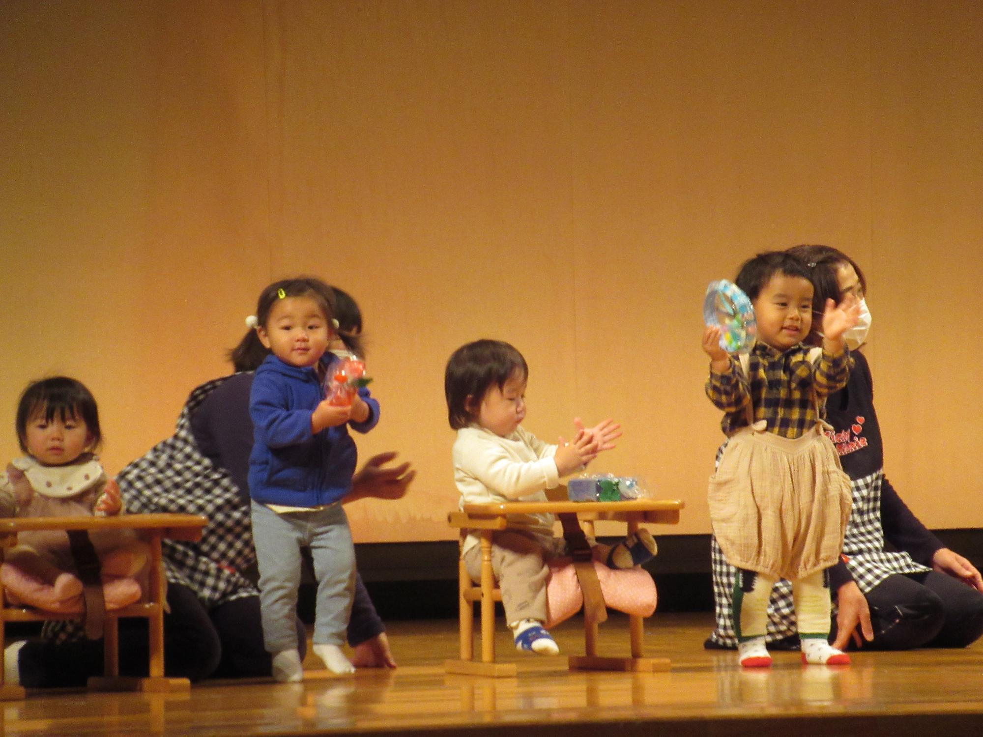 1歳の子どもたち手作り楽器で舞台で合奏中
